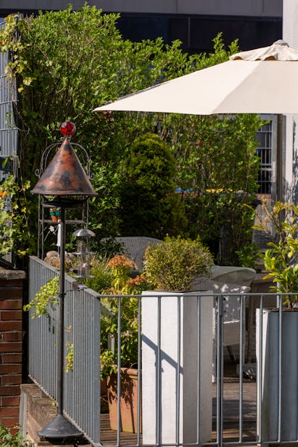 A small urban terrace garden in Shoreditch, London, featuring a variety of lush green plants including shrubbery and small trees within raised planters and along the edges. The area is enclosed by a m
